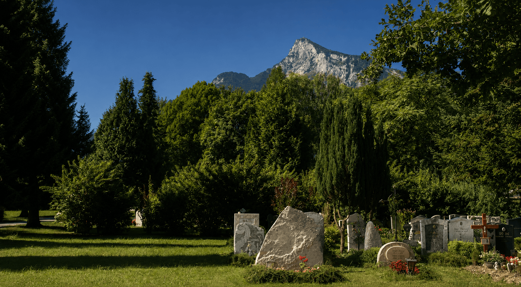 Friedhof mit gepflegten Gräbern im Grünen, im Hintergrund die Berge